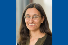 Pictured is Dr. Christina Leslie, PhD, a woman smiling warmly at the camera, with long dark hair and glasses. She is wearing a dark-colored blouse with a lighter, olive-green section near the neckline. The background is blurred, suggesting an indoor setting with natural light.